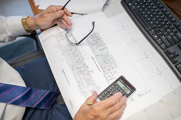A man is sitting at his desk and working with a calculator on building floor plans