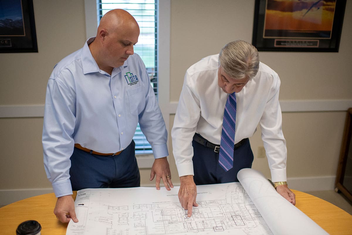 Learn more about our history Brian kaupp and an older man talking and looking at floor building plans and planning