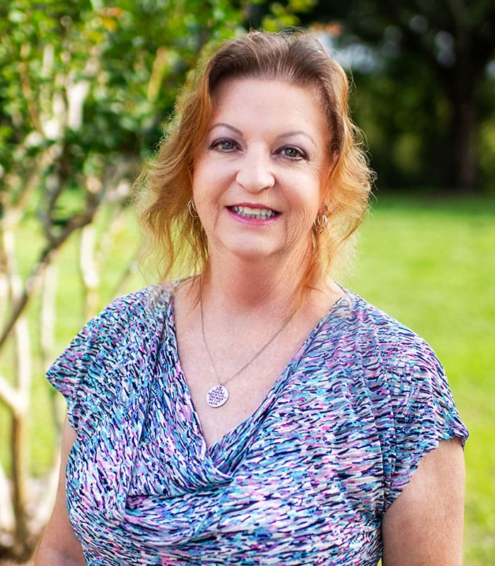 A headshot outdoors image of Lynn Challandes smiling and posing outside