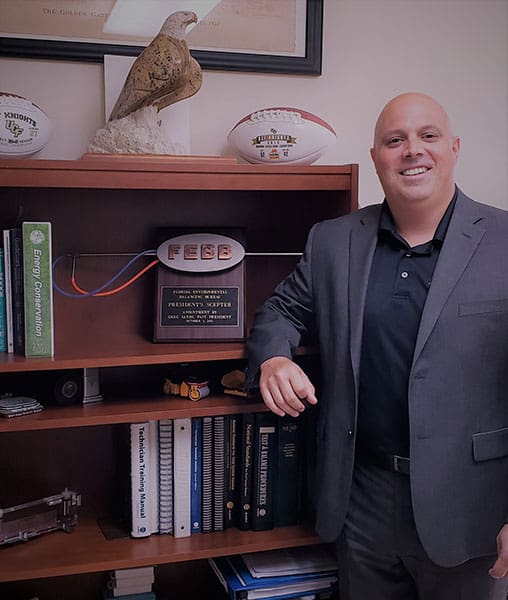 A headshot of Brian Kaupp in front of his shelves with his accomplishments and certificate