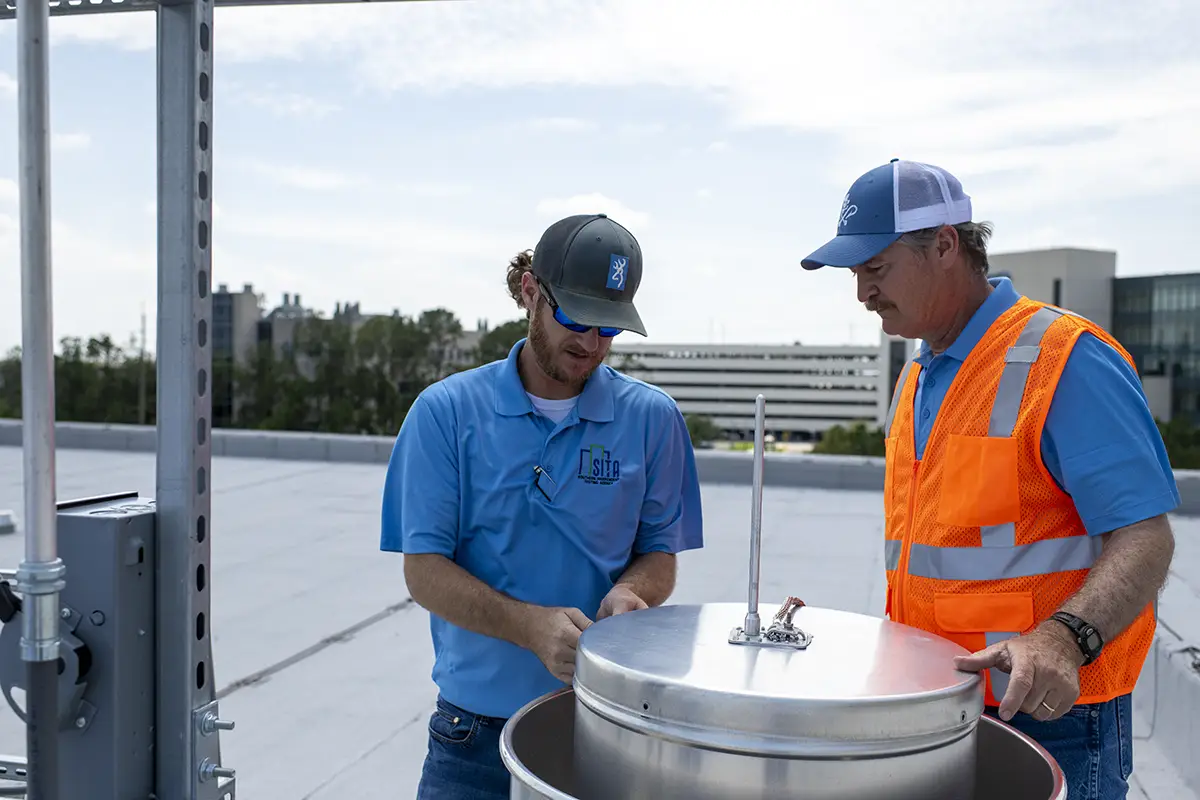 Two men in SITA golf shirts working on building Air Barriers and testing them on the roof of a building