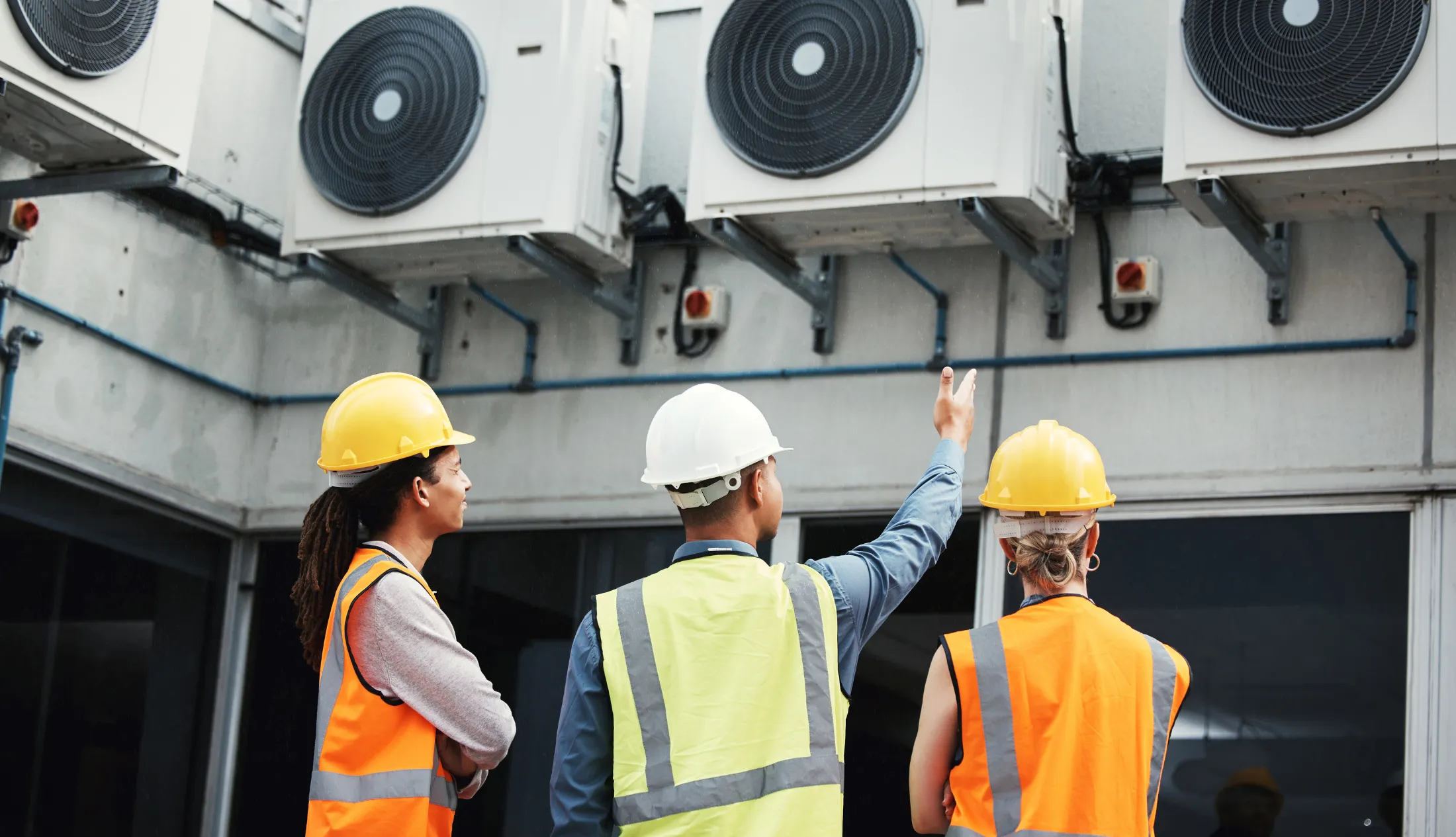 Untitled-2200-x-1265-px-2024-10-16T184516.111 Engineers assessing commercial HVAC units on a building exterior, discussing airflow performance and system balance during a site inspection.