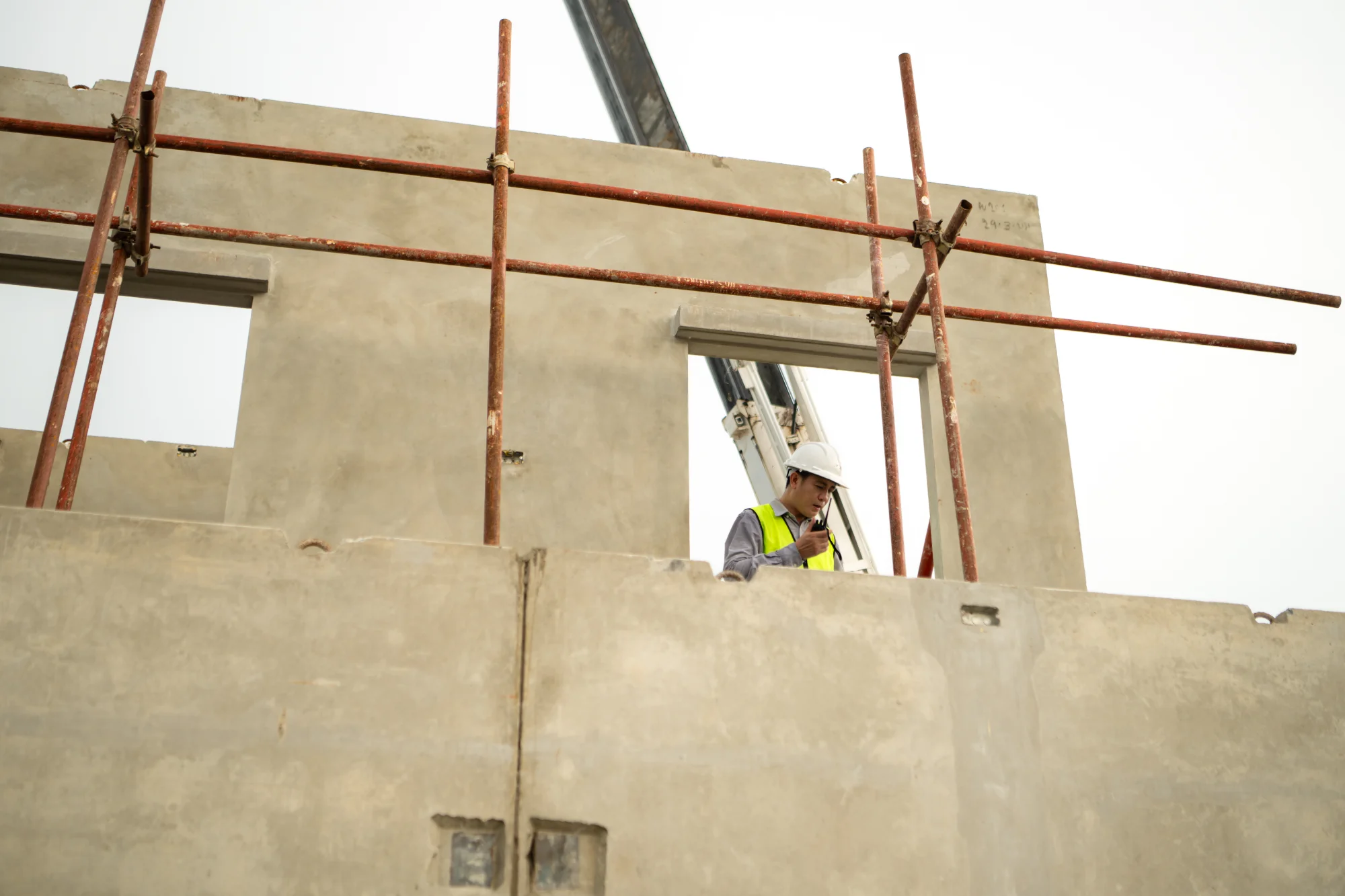 construction-worker-inspecting-building-structure-sita. Construction worker in safety gear inspecting concrete building structure with temporary metal scaffolding and support beams during new building commissioning phase.