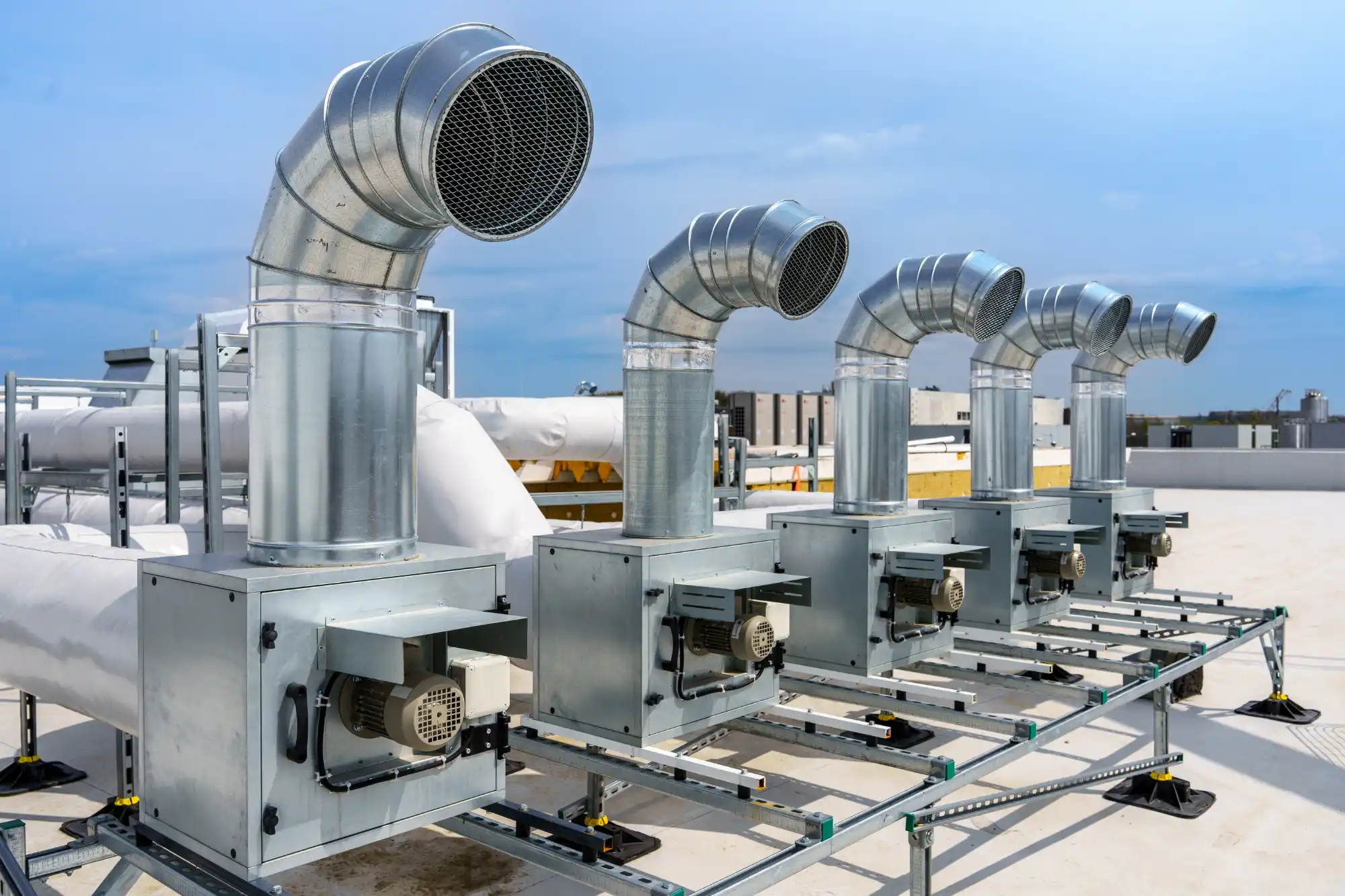 Row of rooftop exhaust fan units with curved galvanized ductwork on a commercial building