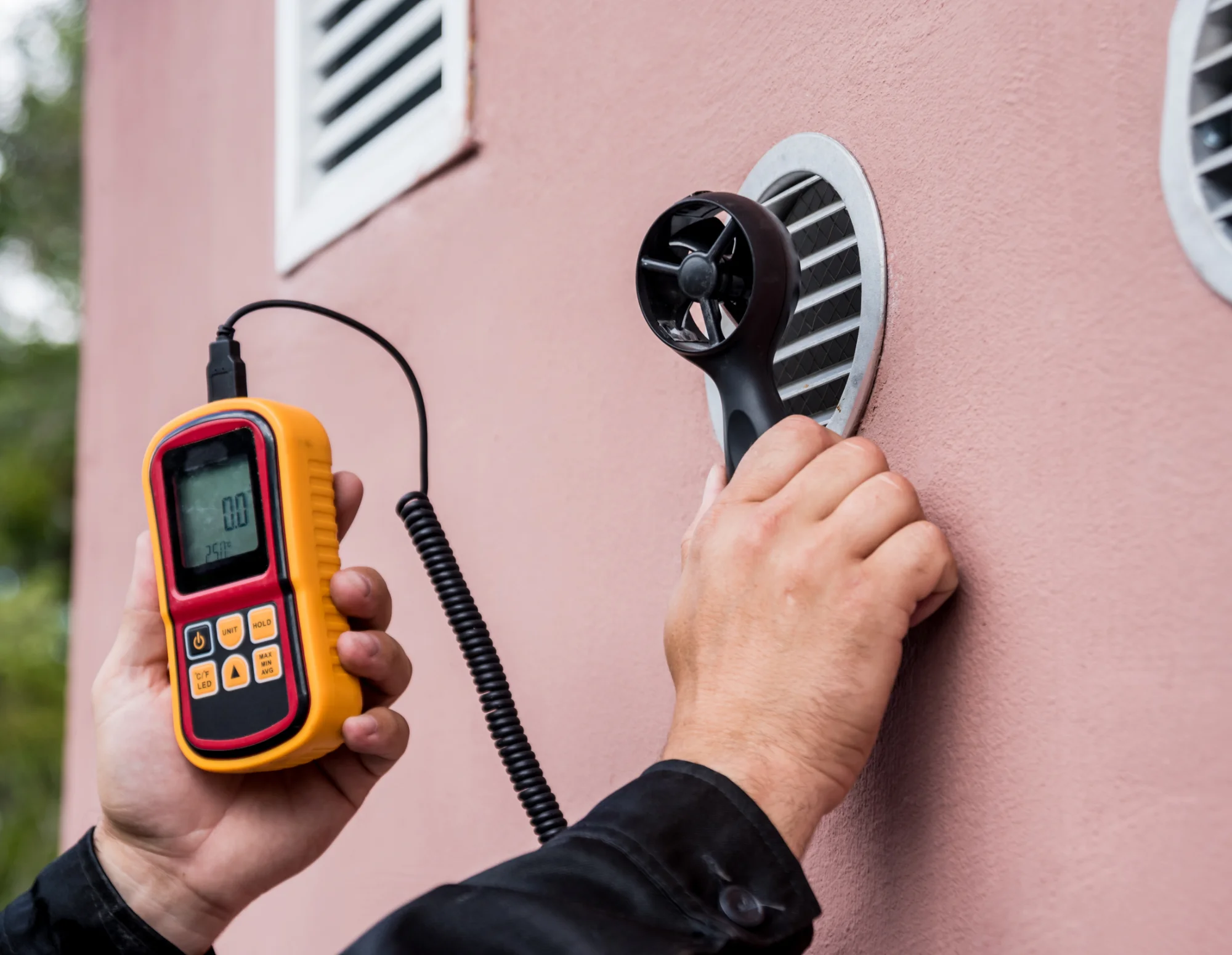 Technician using an anemometer to measure airflow at an exterior wall vent